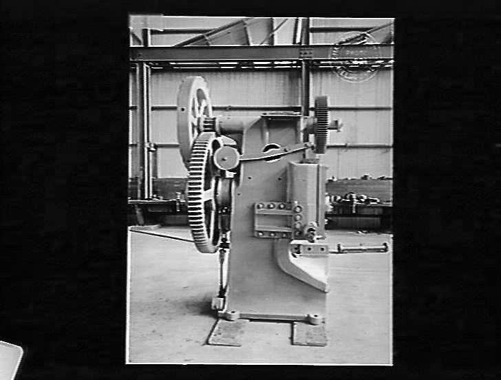 Schwarzes und weißes Foto einer industriellen Automatenmaschine in einer Fabrik mit einer Wand im Hintergrund.