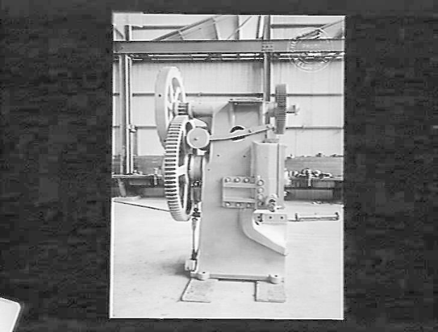 Schwarzes und weißes Foto einer industriellen Automatenmaschine in einer Fabrik mit einer Wand im Hintergrund.