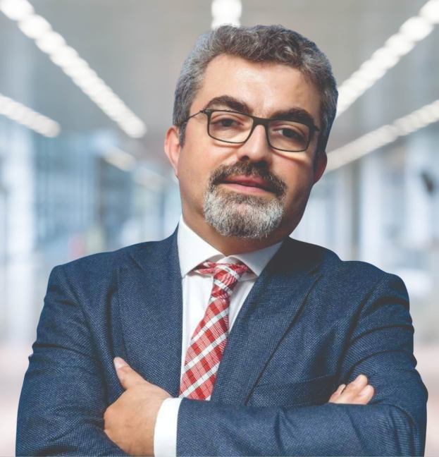 Ein Mann in Anzug und Krawatte mit verschränkten Armen, der eine Brille trägt und vor einem unscharfen Hintergrund steht, mit Text, der ihn als neu ernannte Marketingchef identifiziert.