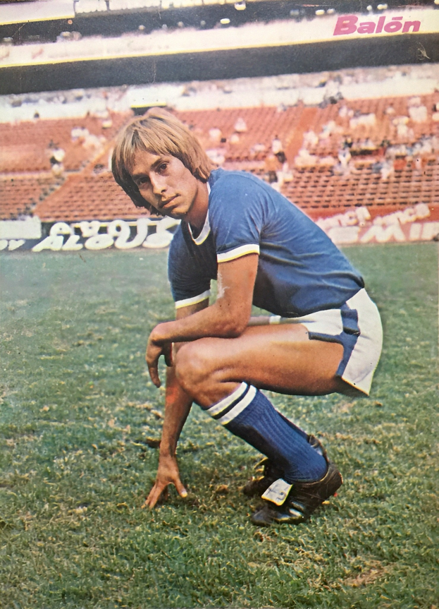 Ein Mann kniet auf einem Fußballfeld umgeben von Menschen, die auf Stühlen und Brettern mit Text sitzen.