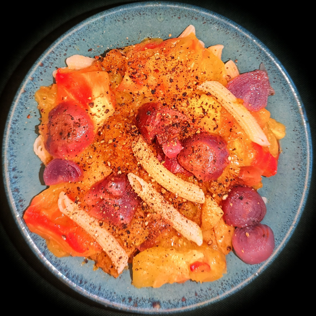 Ein blauer Teller mit einem Gericht aus Sauerkraut, Würstchen, Kartoffeln und Gemüse in einer würzigen Sauce.