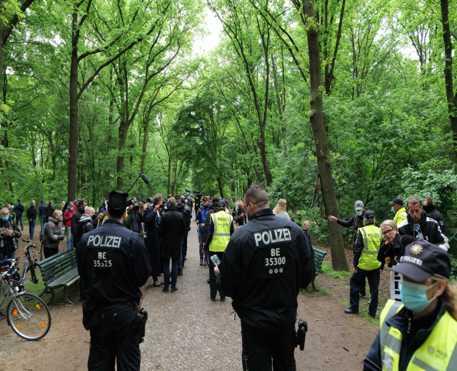 Polizisten vor einer Menge bei einer Outdoor-Veranstaltung mit Fahrrädern und einer Bank im Vordergrund.