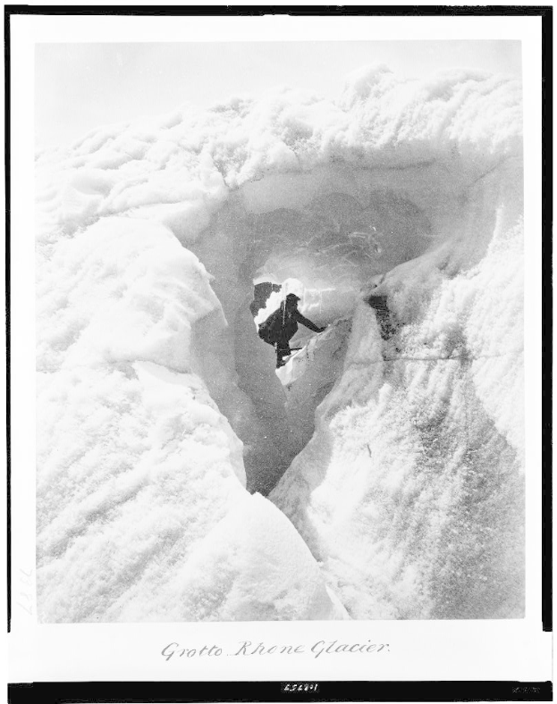 Schwarz-weißes Foto einer Person, die eine schneebedeckte Bergwand hochklettert, mit der Beschriftung "Grotto Rhone Glacier" und schneebedeckten Hängen und Himmel im Hintergrund.