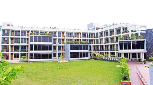Ein großes Gebäude mit einem grünen Rasen, umgeben von Pflanzen, Bäumen und einer Wand, mit einer Treppe zum Eingang und einem Logo, das darauf hinweist, dass es sich wahrscheinlich um die Universität für Wissenschaft und Technologie handelt, unter einem klaren Himmel.