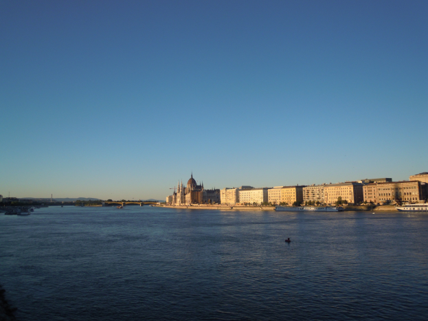 Luftaufnahme des Donauufers in Budapest, Ungarn, mit Booten, Flussufergebäuden mit Fenstern, Bäumen, einer Brücke und einem Himmelhintergrund.
