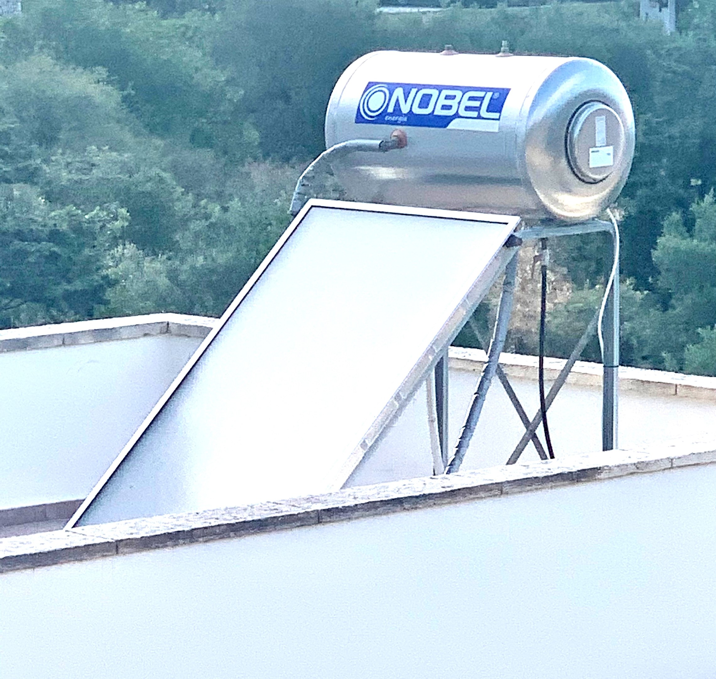 Solarwassererwärmer mit Speicherbehälter auf dem Dach eines Gebäudes montiert, Bäume im Hintergrund sichtbar.