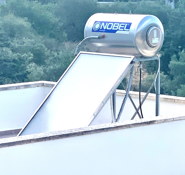 Solarwassererwärmer mit Speicherbehälter auf dem Dach eines Gebäudes montiert, Bäume im Hintergrund sichtbar.